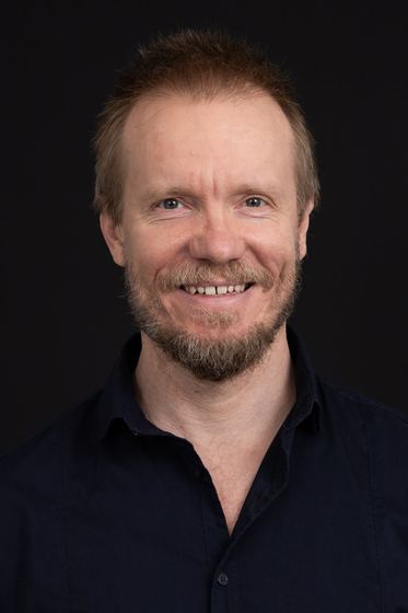Matti Boustedt, smiling studio portrait in navy shirt