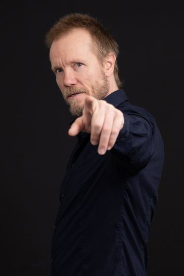 Matti Boustedt, studio portrait in navy shirt, pointing at camera