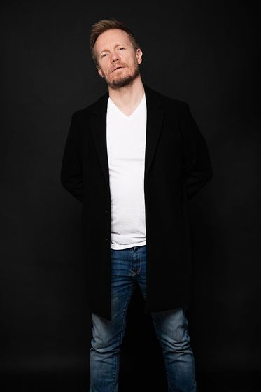 Matti Boustedt, studio portrait in black coat, white t-shirt