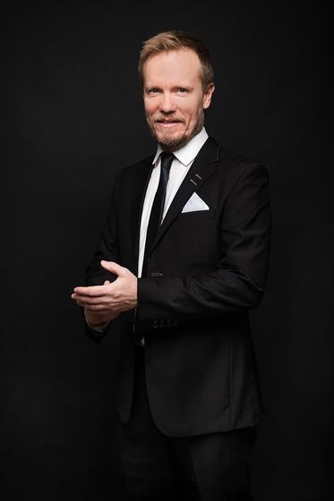 Matti Boustedt, smiling studio portrait in black suit and tie