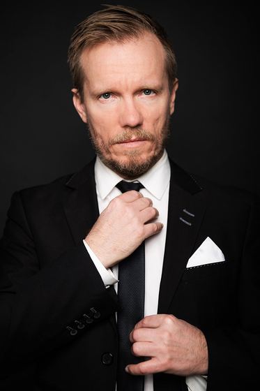 Matti Boustedt, studio portrait adjusting tie, black suit