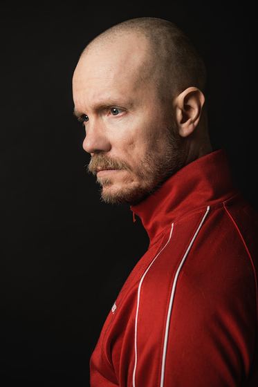 Matti Boustedt, profile character portrait with shaved head, red jacket